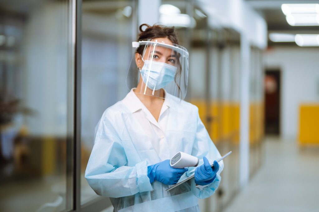 Disease control expert in visor with thermometer equipment to check the temperature at office